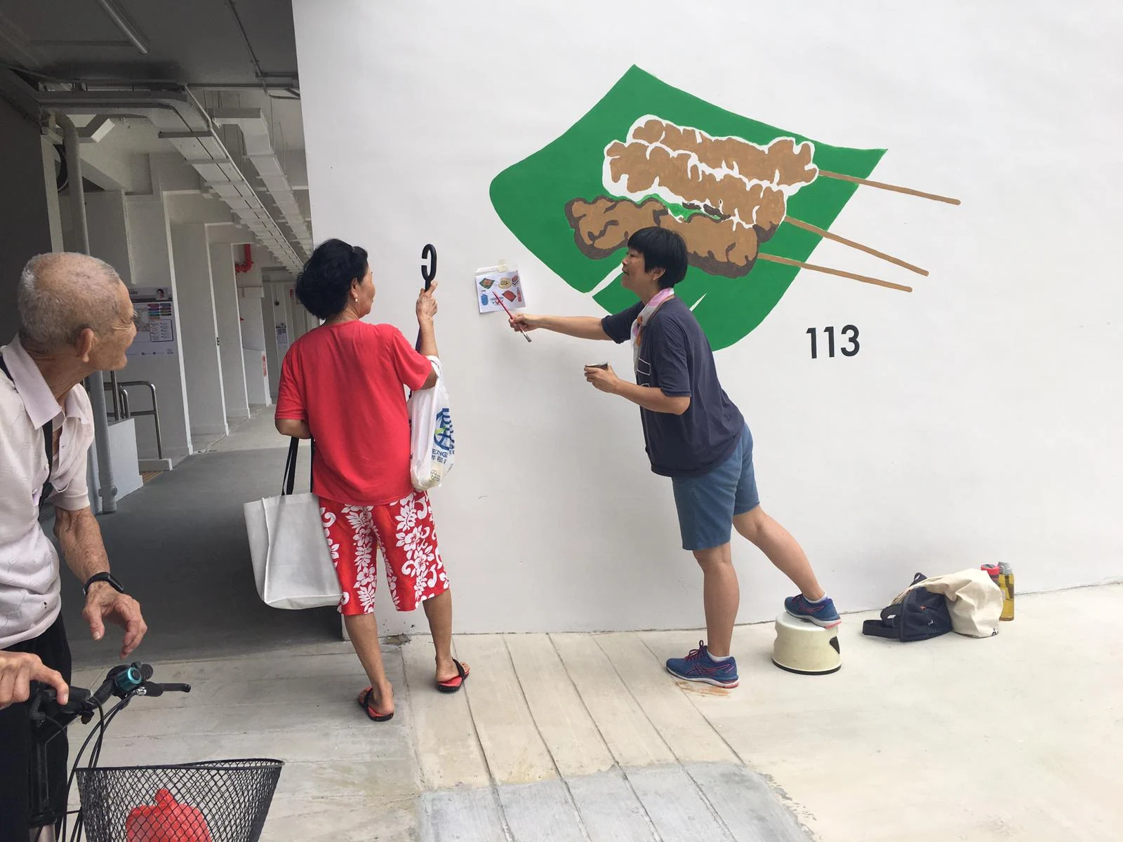 An artist points at a diagram next to a mural in progress on a wall.