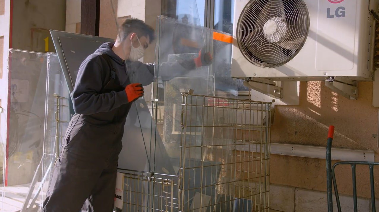 A man puts a pane of glass with other panes of glass inside a metal basket container.