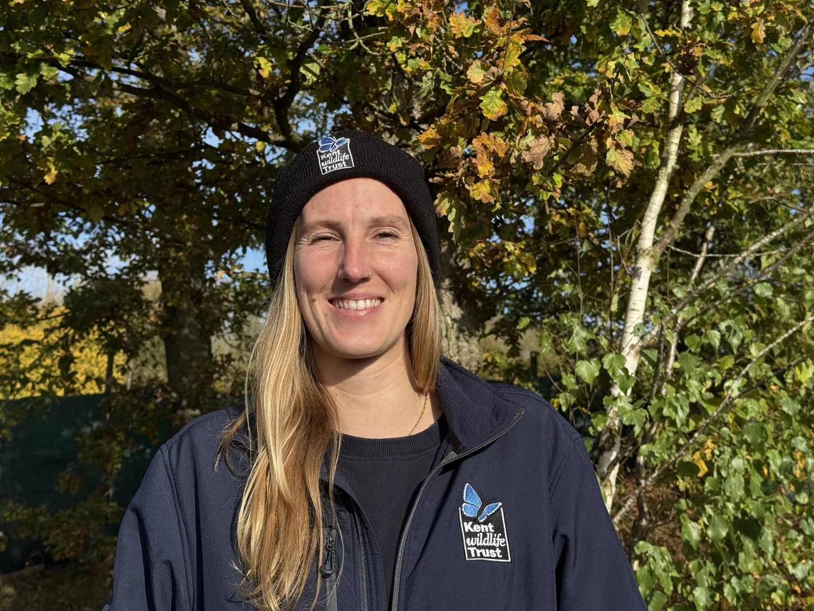 A woman with blond hair wearing a black beanie smiles at the camera.