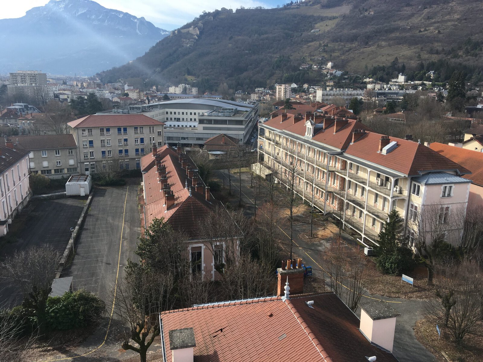 A view of some of the buildings before deconstruction. They are large beige buildings with red roofs. A mountain is visible in the background.