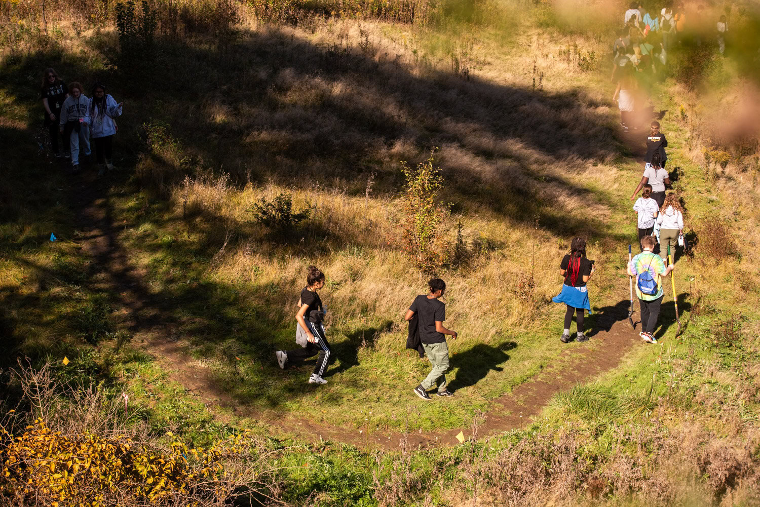 A view from above of people hiking on a trail with shadows cast from trees.