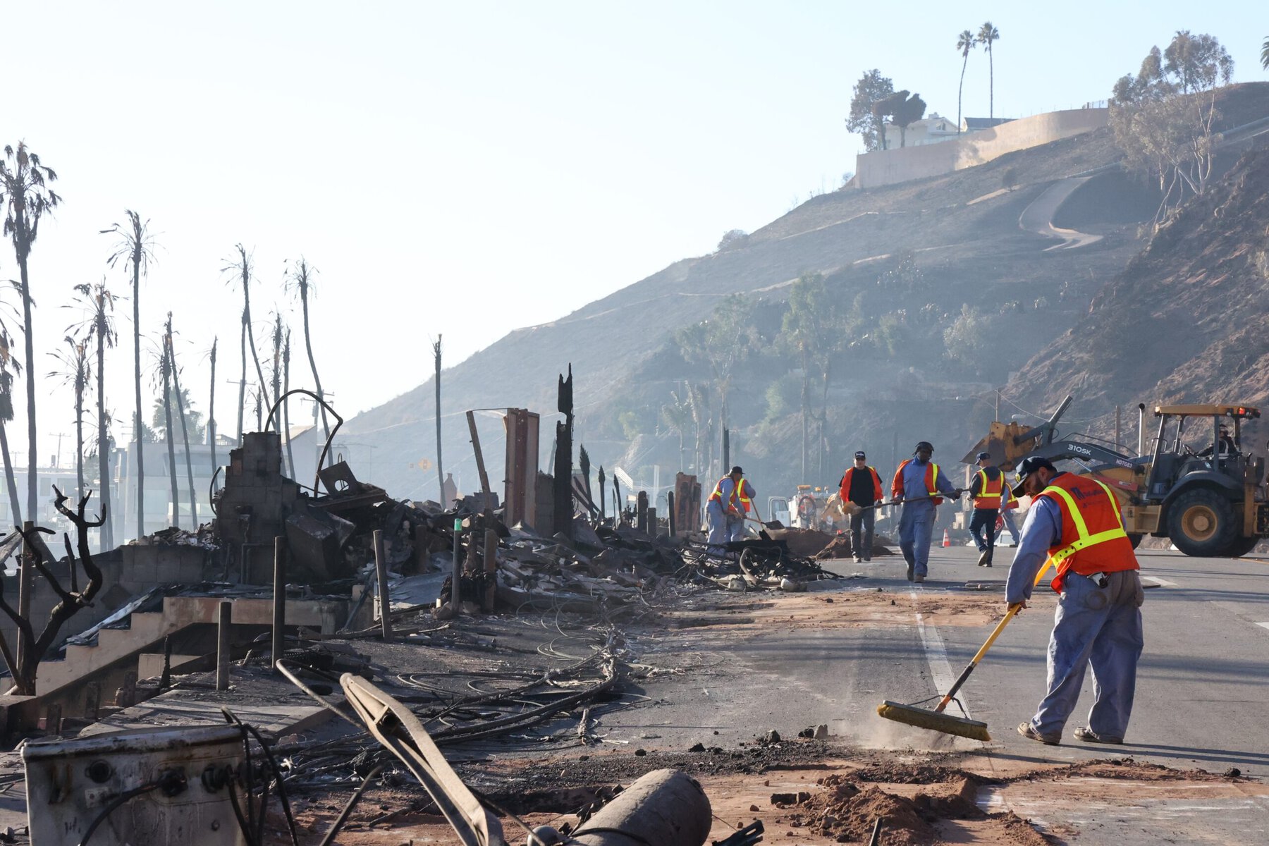 Workers clear the PCH after the Palisades fire burned through.