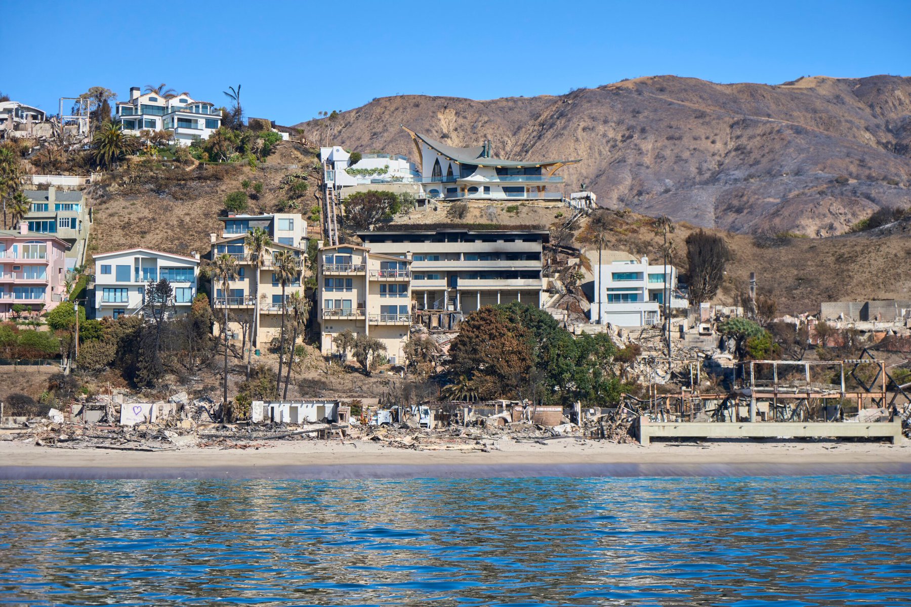 The coastal view after the Palisades Fire. The famous "Eagle's Watch" home designed by Harry Gesner survived as seen in the upper center. Many homes nearby were destroyed.