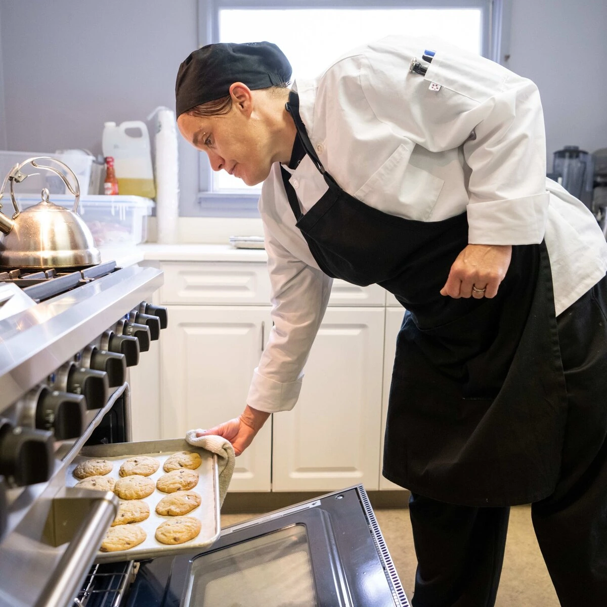 A person in a black and white chef's outfit puts a tray into the oven.