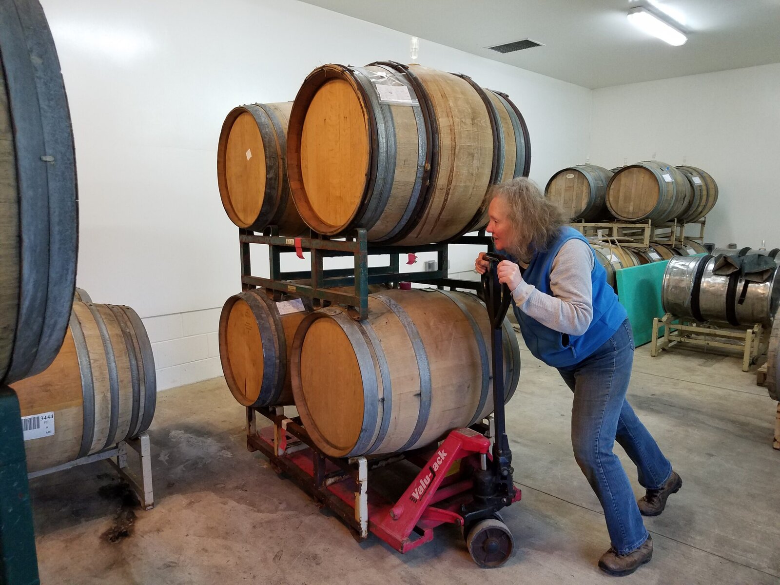 A woman pushes a dolly carrying four casks of wine.