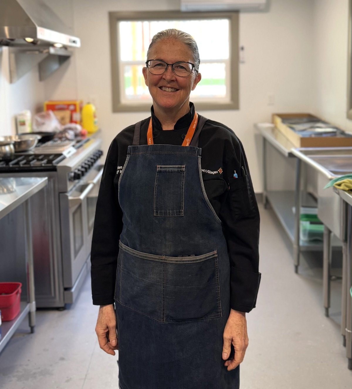Chef Helen Coyne stands in a kitchen wearing and apron, smiling.