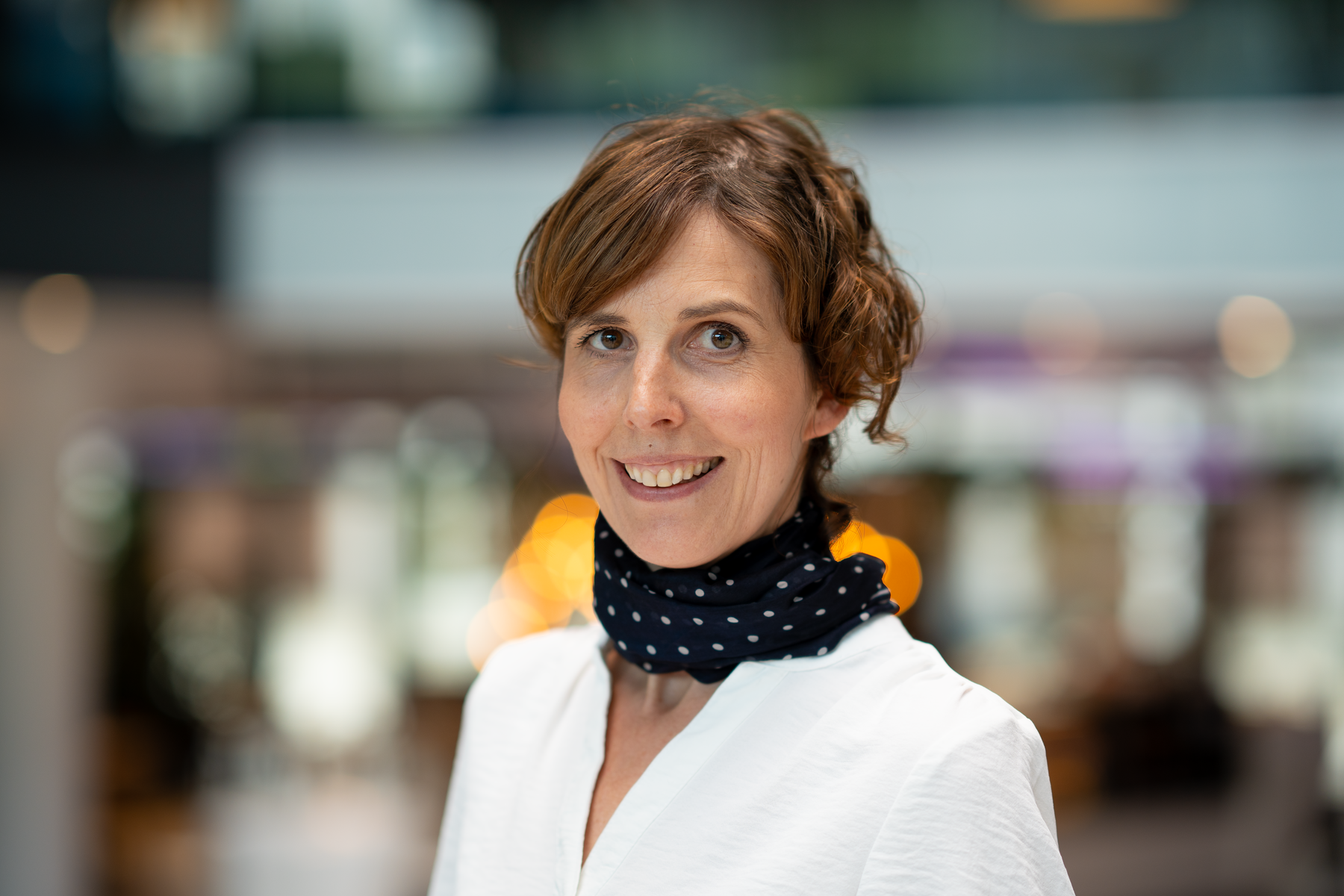 Managing editor Camilla Kvalheim smiles at the camera. She is wearing a white shirt and black scarf and her broad hair is pulled back.