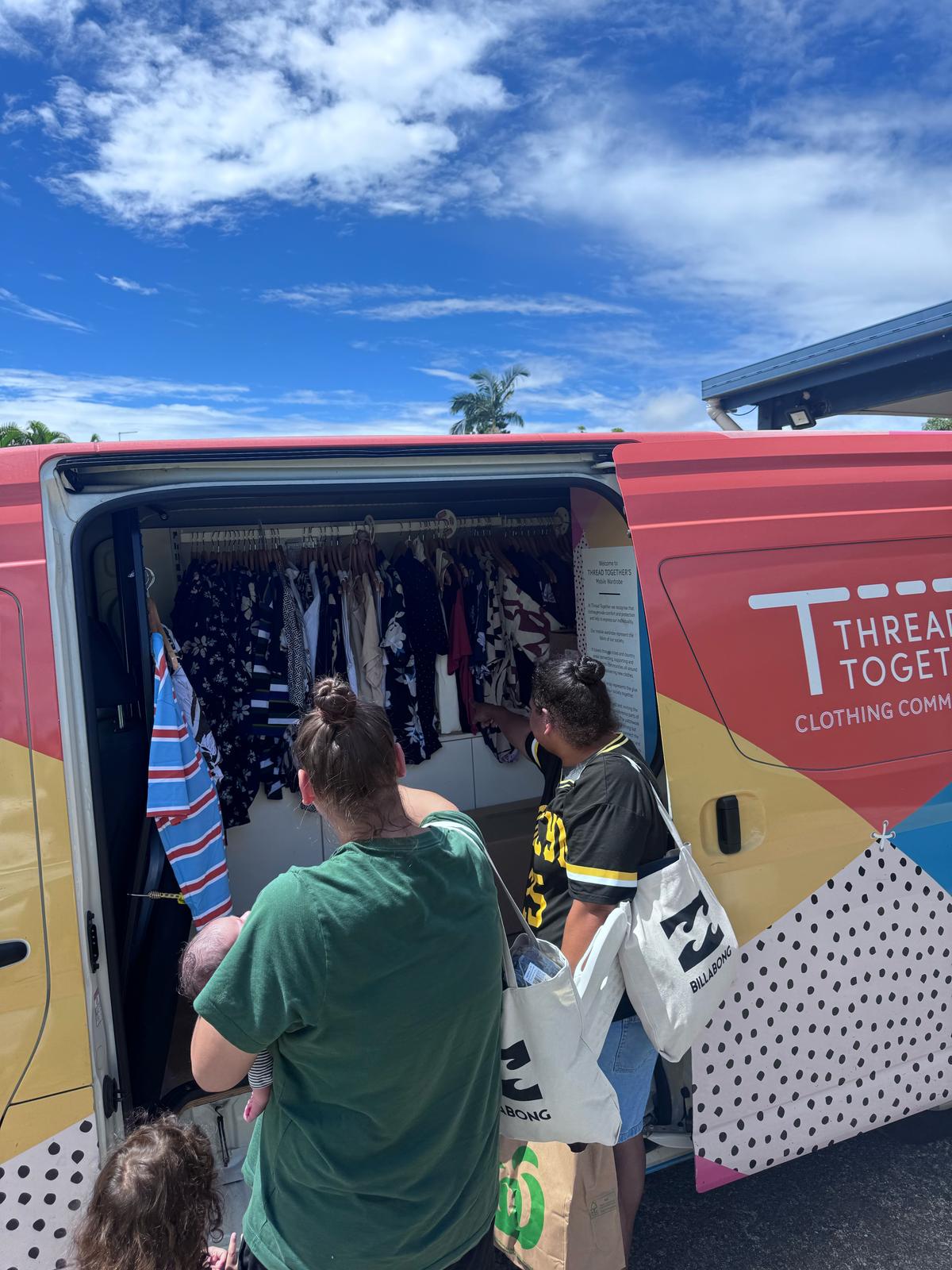 People browse clothes on a rack inside a Thread Together van.