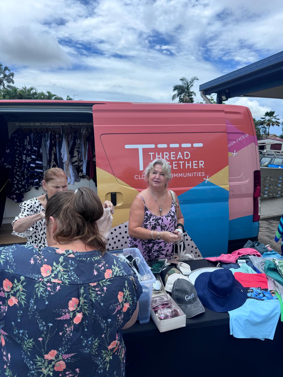 Two women give out clothes in front of a Thread Together van.