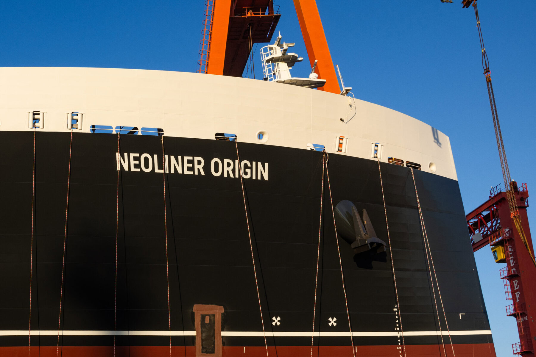 A close-up of the outside of a large ship called the Neoliner Origin. It is black and white with a red crane behind it.