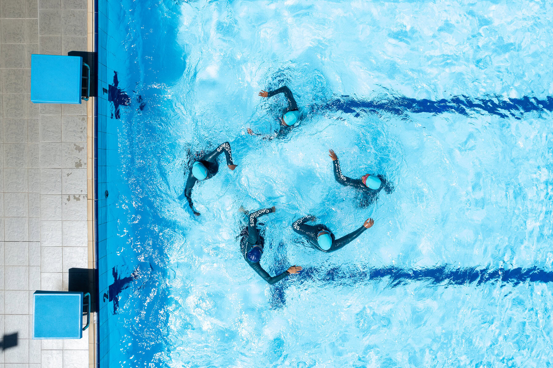 An aerial view of a group of young women standing in a circle in a swimming pool.