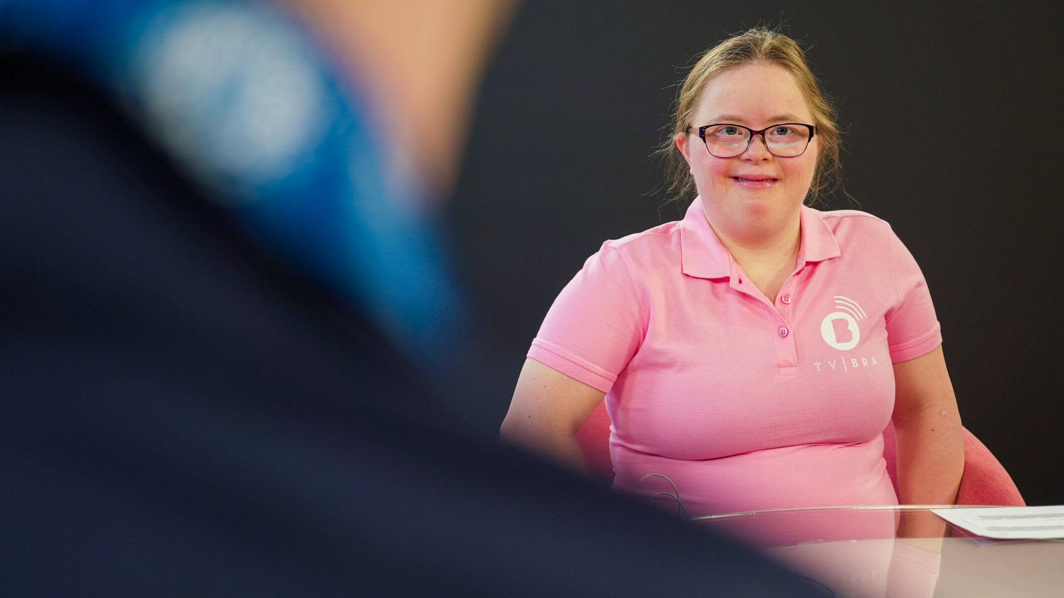 Emily Ann Reidel in the studio. She wears glasses and a pink polo shirt.