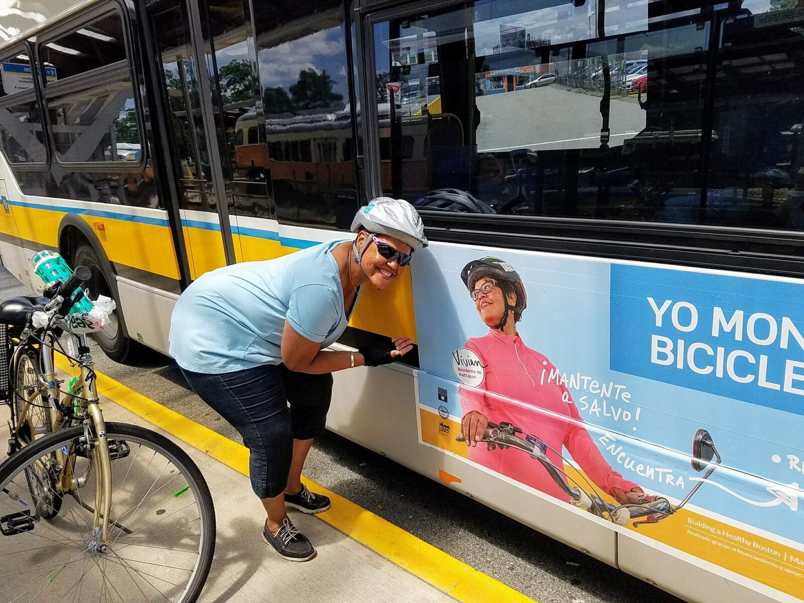 Vivian Ortiz, wearing a bike helmet and sunglasses, poses next to a picture of herself on a city bus.