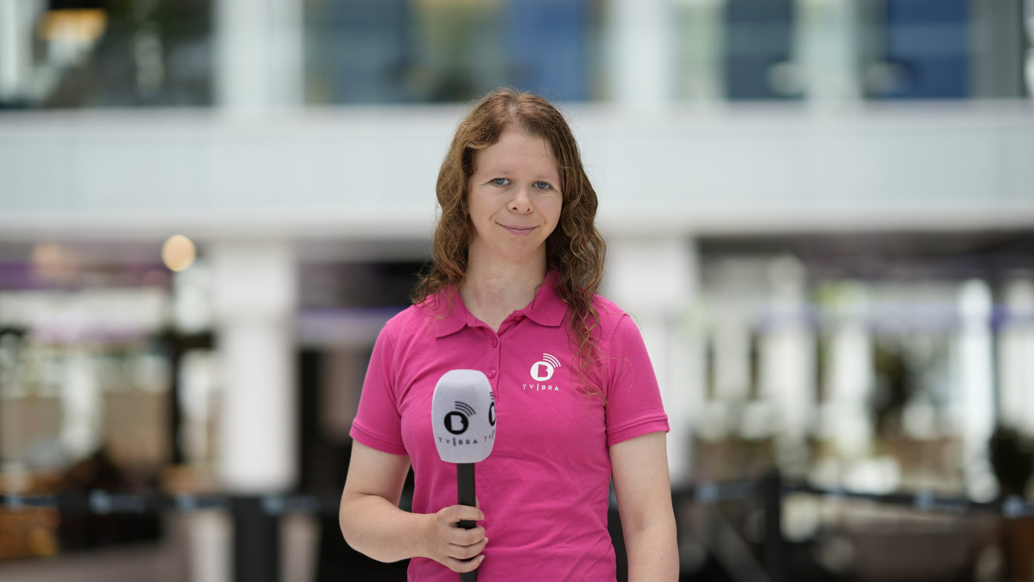 Reporter Lisa Bergen holds a microphone. The space behind her is blurry but could be an office or government building.