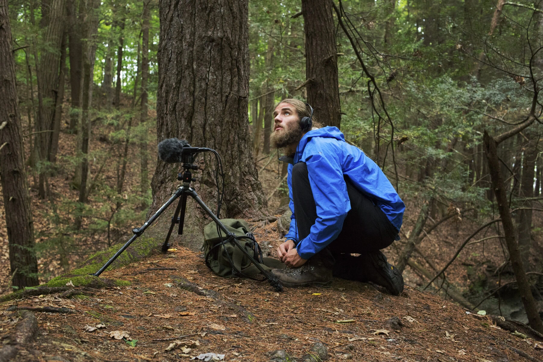 Matt Mikkelson recording natural noise. He is crouched in the woods next to a recording device.