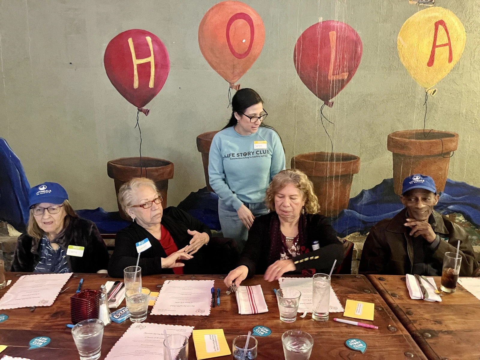 Older people sit at a table at a restaurant with paper and notecards in front of them.